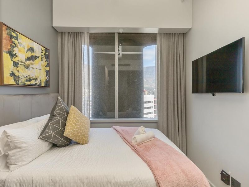A compact, well-maintained bedroom featuring a large window with curtains and a wall-mounted television setup.