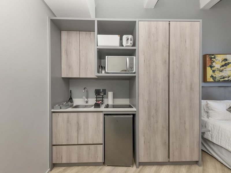 A compact, modern kitchenette unit featuring light wood-grain cabinetry, a stainless steel sink, and a built-in cooktop, integrated into a bedroom space.