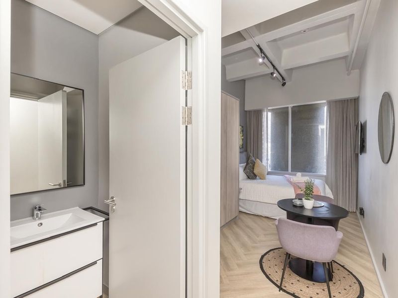 A modern bedroom featuring herringbone flooring, track lighting, and an en-suite vanity area with a contemporary basin and mirror.
