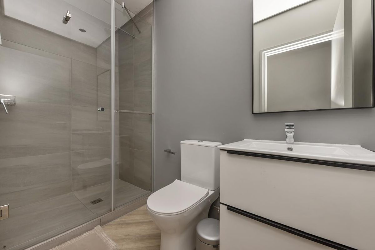 Modern bathroom featuring a walk-in shower with glass enclosure, contemporary vanity with basin, and a wall-mounted mirror in a neutral grey color scheme.