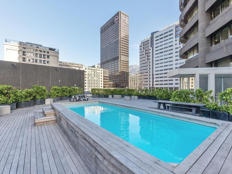 A well-maintained rooftop pool area featuring raised timber decking, integrated planters, and expansive urban city views.