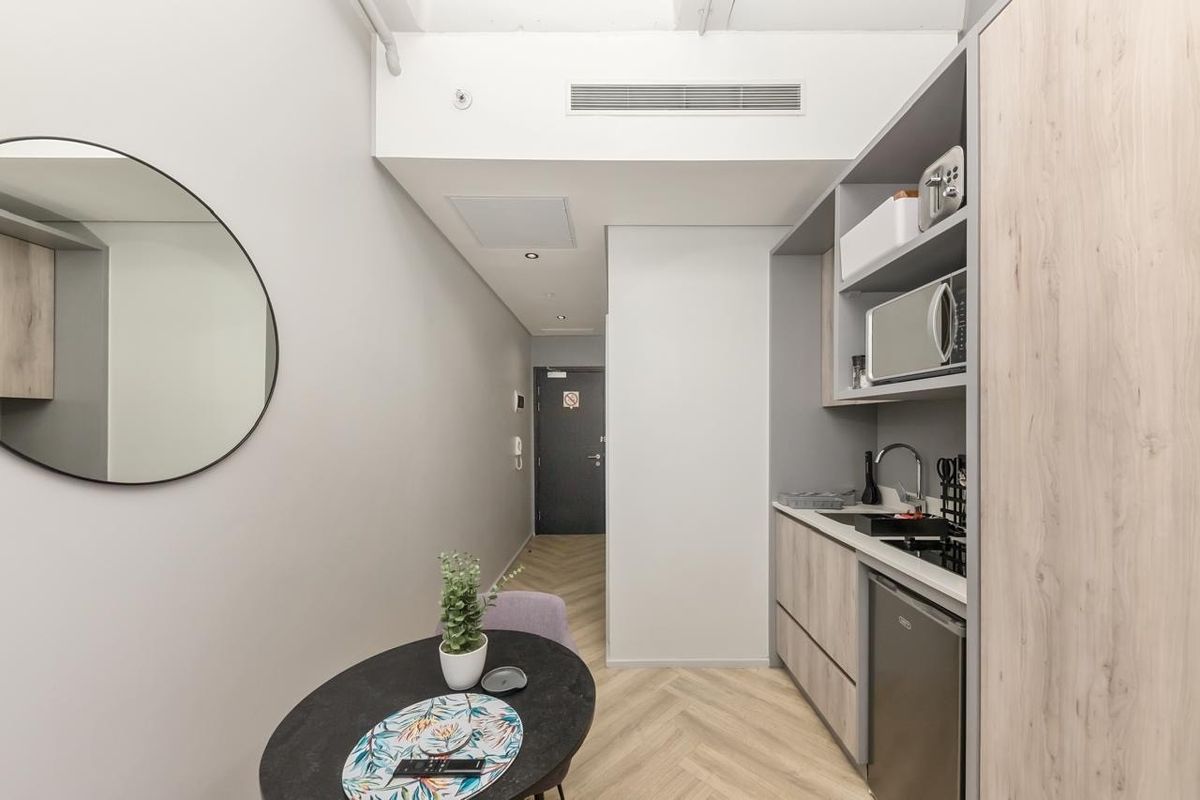 Compact modern kitchen featuring built-in cabinetry, integrated microwave, sink, and stylish herringbone flooring, leading into the main entrance hallway.