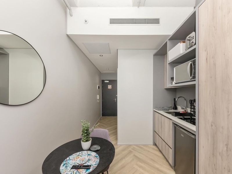 Compact modern kitchen featuring built-in cabinetry, integrated microwave, sink, and stylish herringbone flooring, leading into the main entrance hallway.