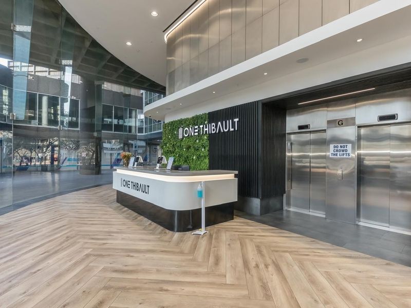 Modern building lobby featuring a reception desk, vertical garden wall, stainless steel elevators, and high-quality herringbone flooring in a contemporary commercial space.