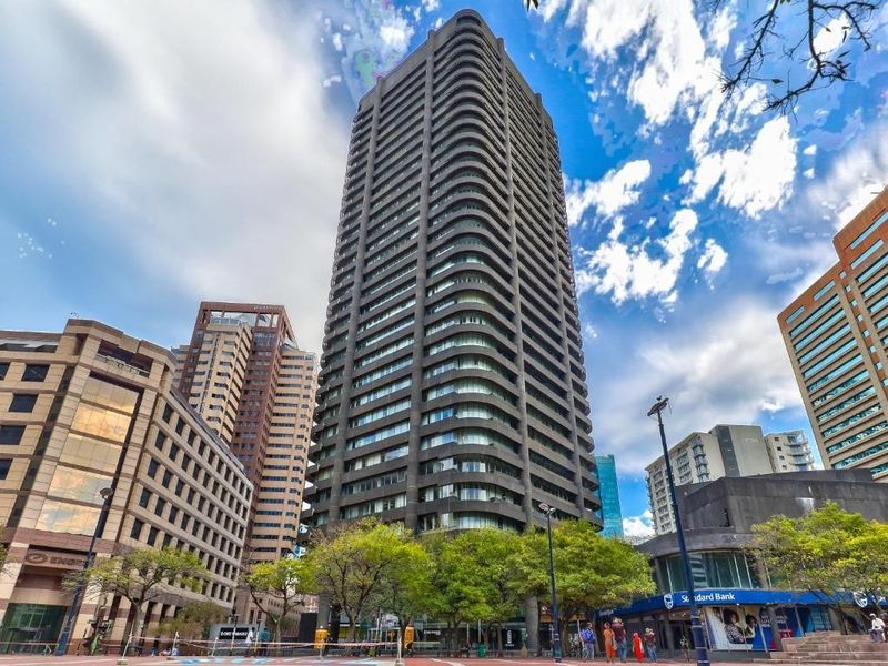 A prominent high-rise residential or commercial building featuring a modern concrete facade with integrated balconies and extensive glass windows in an urban setting.