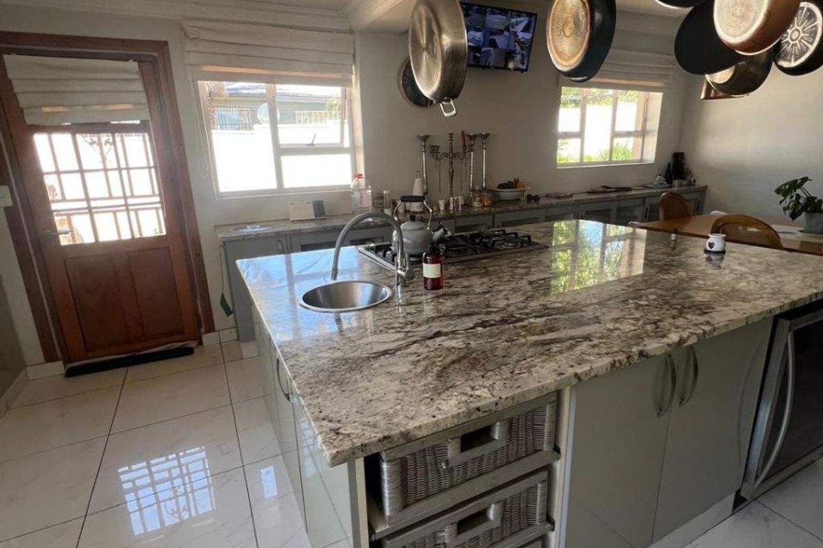 Modern kitchen featuring a large granite island with integrated gas hob, overhead pot rack, tiled flooring, and ample built-in cabinetry.