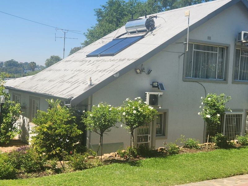 Rear view of the house featuring a solar water heating system, multiple air conditioning units, and a landscaped garden with a paved walkway.