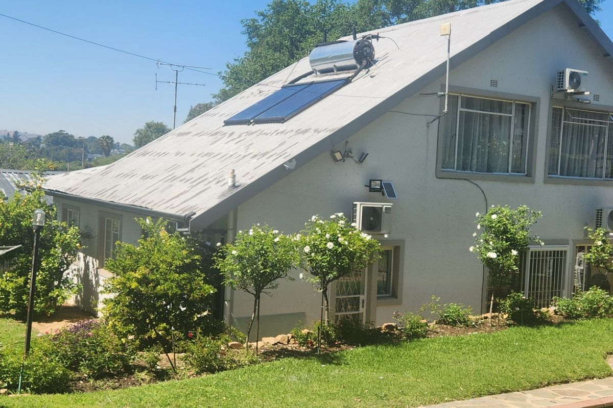 Rear view of the house featuring a solar water heating system, multiple air conditioning units, and a landscaped garden with a paved walkway.