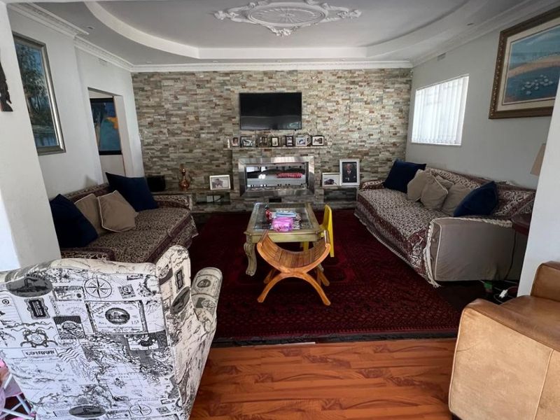 Spacious living room featuring a stone accent wall, built-in fireplace, recessed ceiling with decorative rose, and warm-toned laminate flooring.
