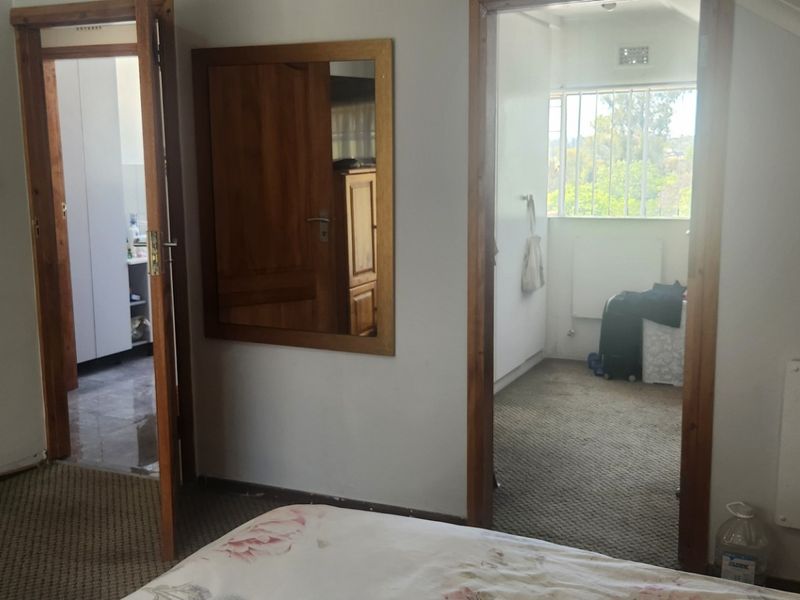 A bedroom featuring carpeted flooring, wooden door frames, and a wall-mounted electric heater, with access to adjacent rooms.