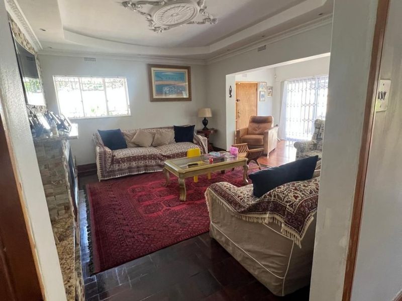 Spacious living room featuring a stone fireplace, decorative ceiling rose, recessed lighting, and dark parquet flooring, offering a classic and comfortable living space.