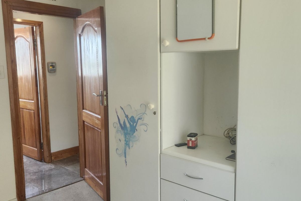 A bedroom featuring built-in cupboards and wooden door frames, leading into an adjacent hallway with tiled flooring.