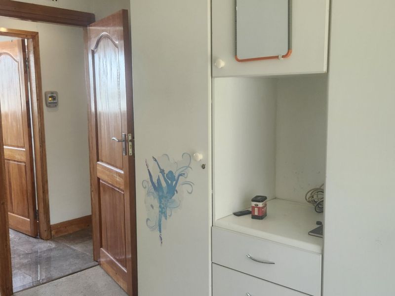 A bedroom featuring built-in cupboards and wooden door frames, leading into an adjacent hallway with tiled flooring.
