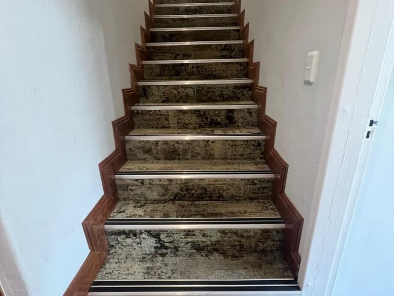 A straight staircase featuring carpeted treads with protective metal nosing and timber skirting boards, leading to an upper level.