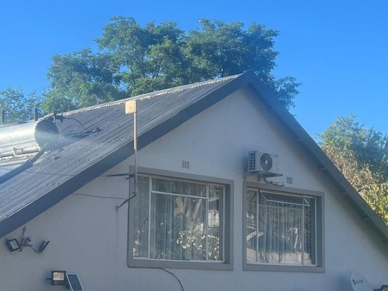 Rear elevation of the house featuring a corrugated metal roof, solar water heating system, multiple air conditioning units, and security window bars.