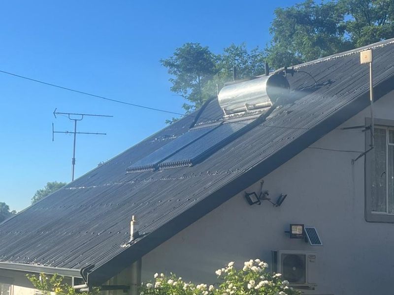Rear view of the property featuring a corrugated metal roof equipped with a solar water heating system and external air conditioning unit.