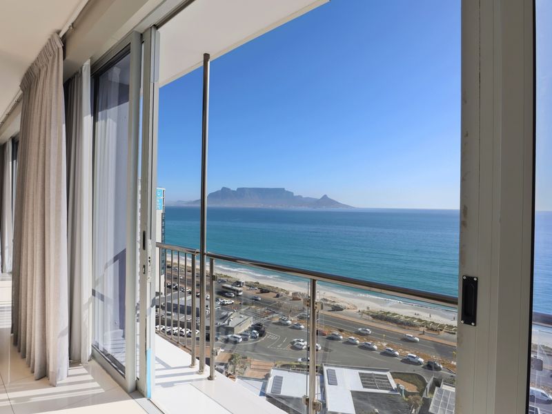 A modern balcony featuring a sleek glass balustrade and stainless steel railing, offering expansive, unobstructed views of the ocean and Table Mountain.