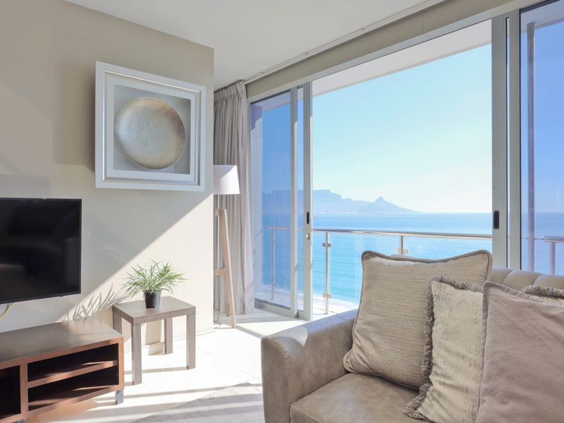 Bright living room featuring large sliding glass doors that open to a balcony with stunning ocean and mountain views.