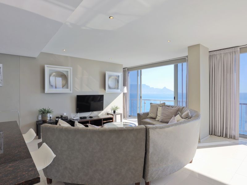 Spacious open-plan living area featuring modern tiled floors, recessed lighting, and large sliding glass doors opening to a balcony with stunning ocean views.
