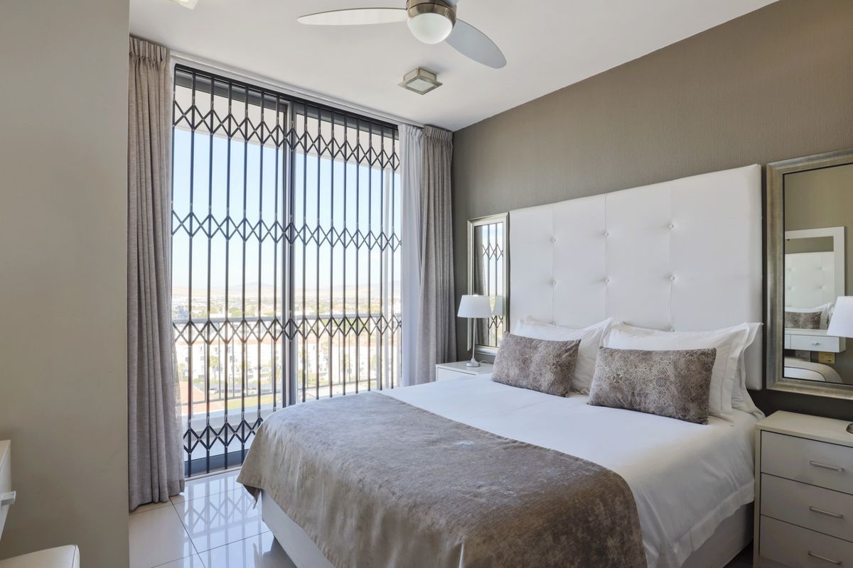 A well-maintained bedroom featuring tiled flooring, a ceiling fan, and a large sliding glass door with an integrated security gate providing balcony access.