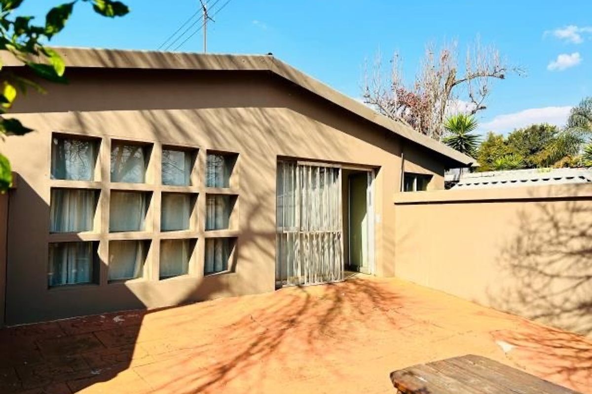 Rear exterior view of the property featuring a paved patio area, grid-pattern windows, and a sliding glass door with a security gate.