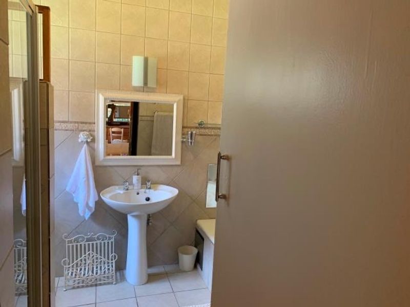A functional bathroom featuring a pedestal basin, wall-mounted mirror, and tiled finishes, providing a clean and practical space.