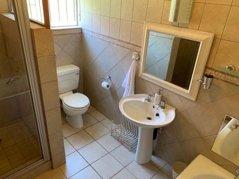 A functional bathroom featuring a pedestal basin, toilet, and a glass-enclosed shower with neutral wall and floor tiling.