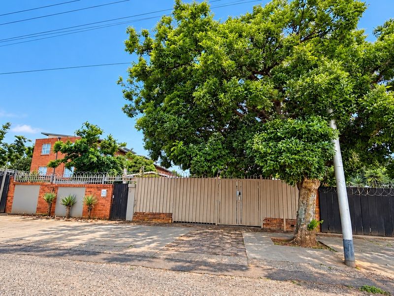Front exterior view of the property featuring a secure gated entrance, brick boundary wall with razor wire, and a paved driveway.