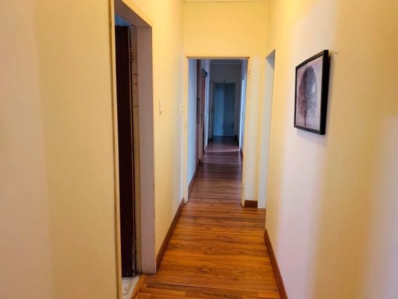A clean, functional hallway featuring laminate wood flooring and neutral wall finishes, providing access to multiple rooms within the home.