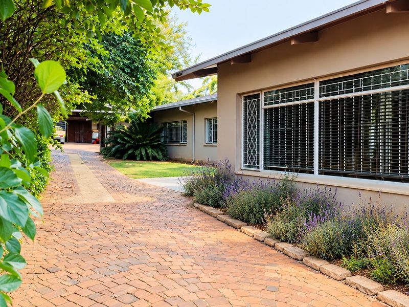 A well-maintained front exterior view featuring a brick paved driveway, landscaped garden borders, and secure window treatments.