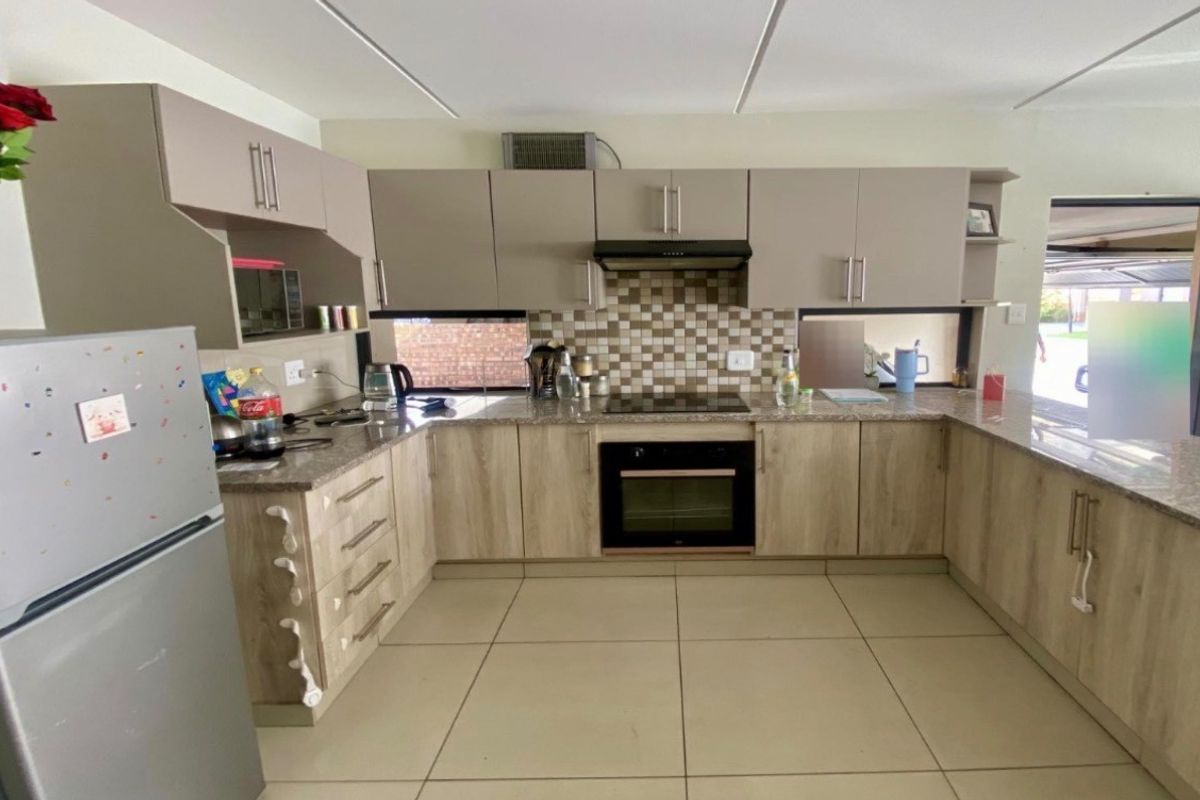 A functional U-shaped kitchen featuring modern wood-look cabinetry, granite countertops, a mosaic tile backsplash, and integrated cooking appliances.