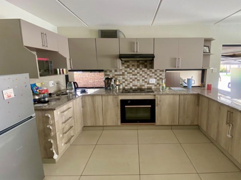 A functional U-shaped kitchen featuring modern wood-look cabinetry, granite countertops, a mosaic tile backsplash, and integrated cooking appliances.