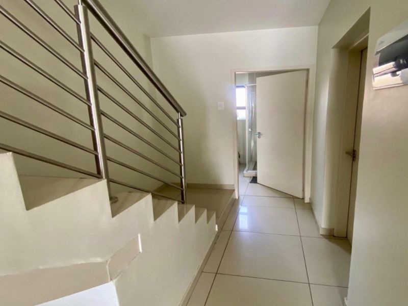 A clean, tiled hallway featuring a modern stainless steel staircase railing and access to an adjacent bathroom.
