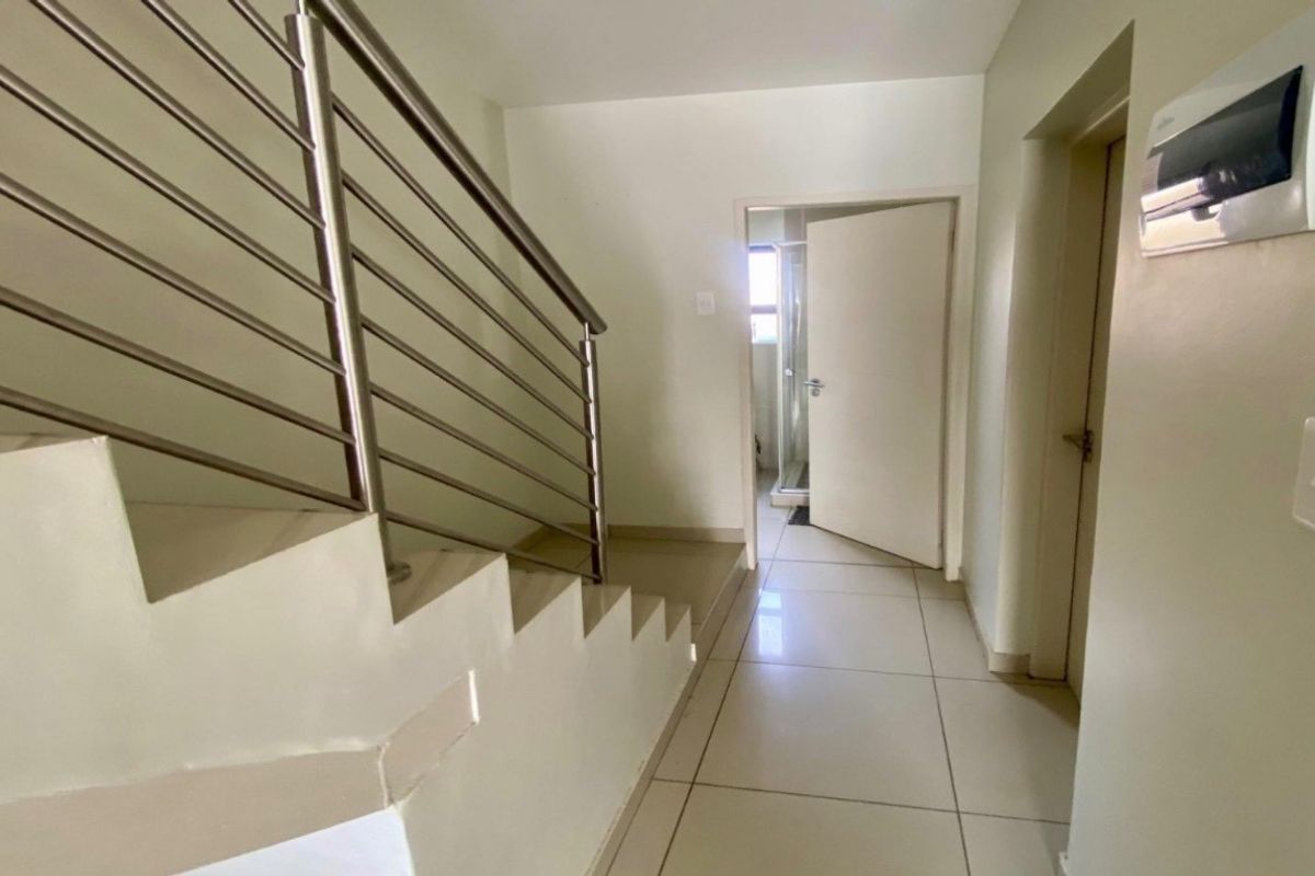 A clean, tiled hallway featuring a modern stainless steel staircase railing and access to an adjacent bathroom.