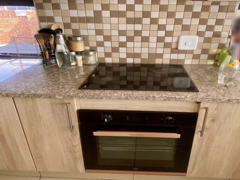 A functional kitchen area featuring a built-in oven, electric hob, laminate cabinetry, and a mosaic tile backsplash with a granite-look countertop.