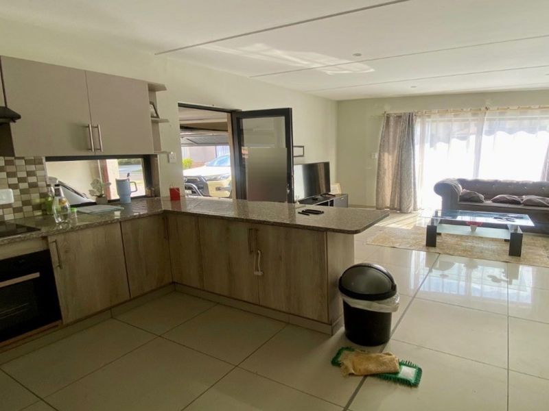 Open-plan living area featuring a modern kitchen with granite countertops, built-in oven, and tiled flooring, seamlessly flowing into a bright lounge space.