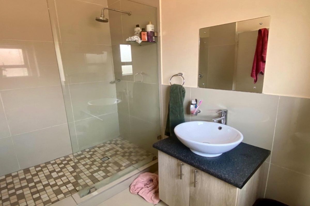 A modern bathroom featuring a glass-enclosed shower with a rain shower head, a vessel sink on a granite vanity, and neutral wall tiling.