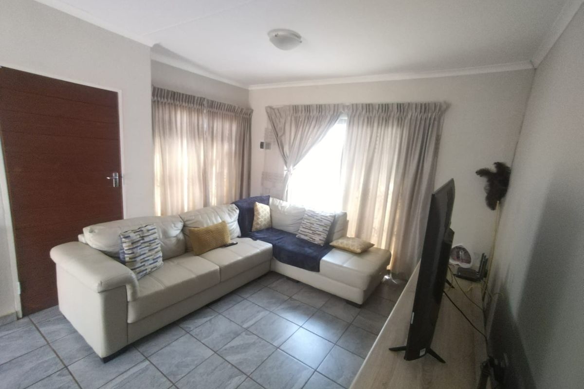 A comfortable living room featuring tiled flooring and large windows with curtain tracks, providing a bright and functional space for relaxation.