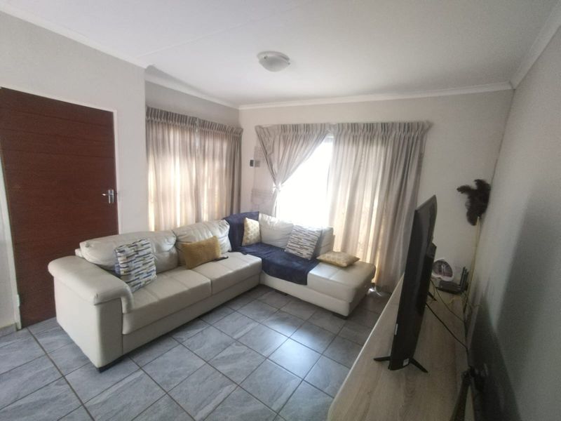 A comfortable living room featuring tiled flooring and large windows with curtain tracks, providing a bright and functional space for relaxation.