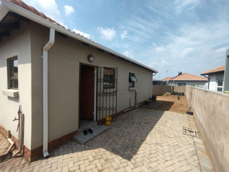 Rear exterior view of the house featuring a paved patio area, security gate, and perimeter walling with an unlandscaped backyard.