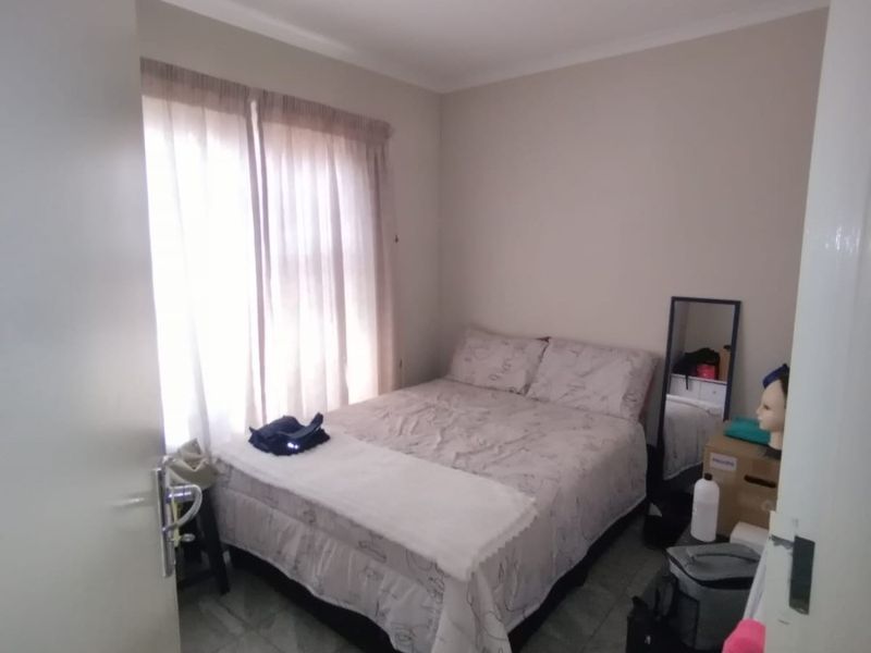 A compact bedroom featuring tiled flooring and natural light through window curtains.