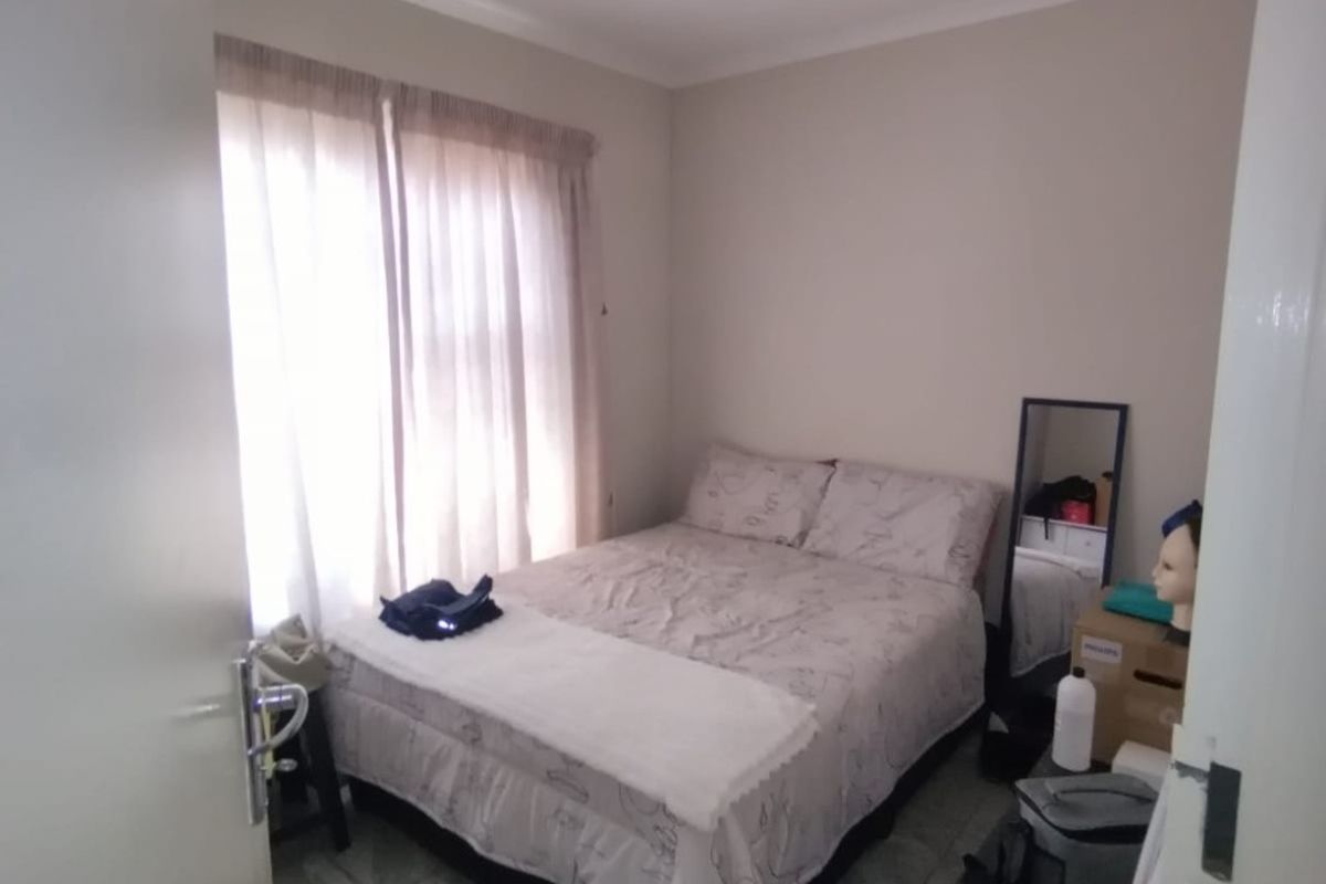 A compact bedroom featuring tiled flooring and natural light through window curtains.