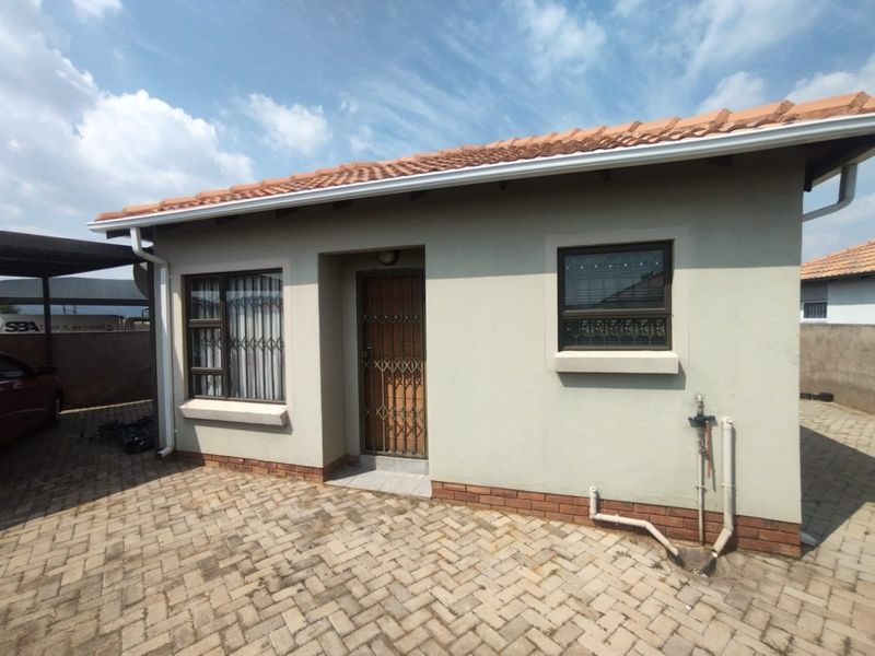 Front elevation of a single-story house featuring a tiled roof, brick paved driveway, and secure aluminium window frames with security gates.