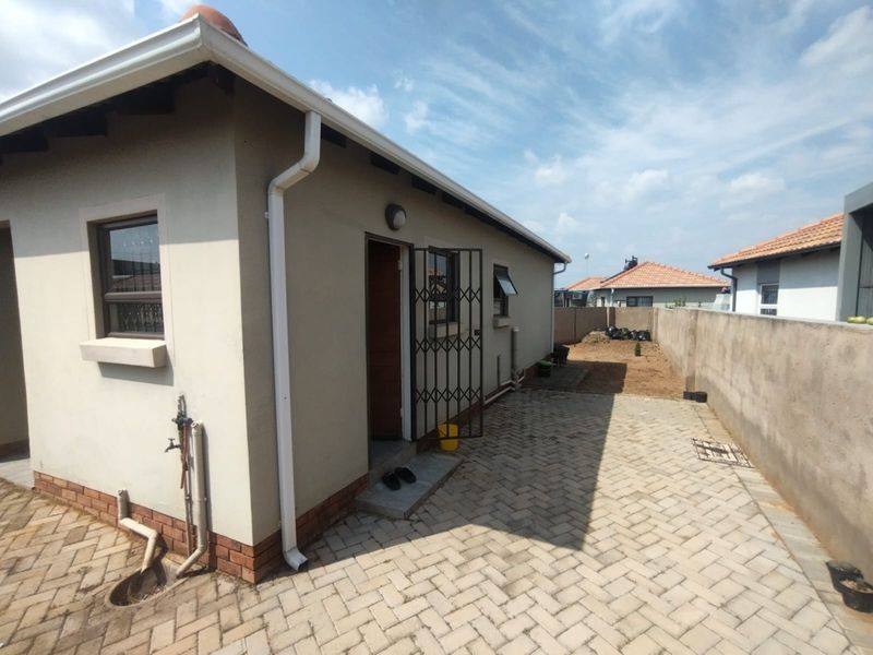 Rear exterior view of the property featuring a paved patio area, boundary wall, and functional gutter system.