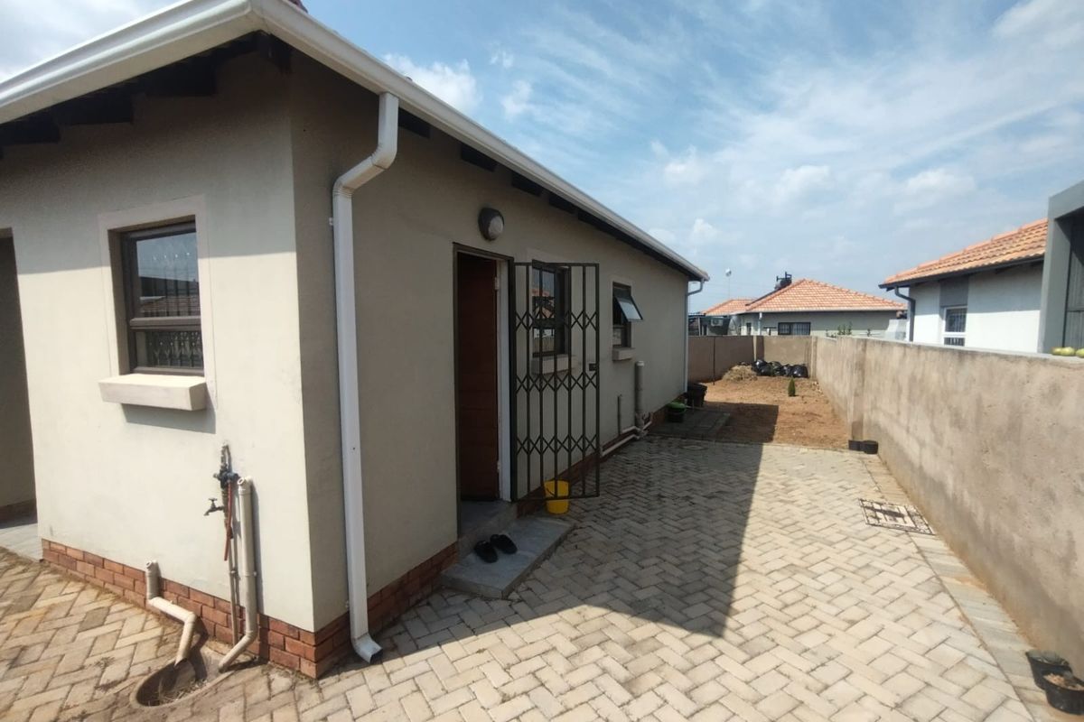 Rear exterior view of the property featuring a paved patio area, boundary wall, and functional gutter system.