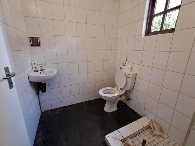 A functional guest bathroom featuring a wall-mounted basin, toilet, and tiled finishes, requiring cosmetic updates to improve its overall aesthetic and condition.