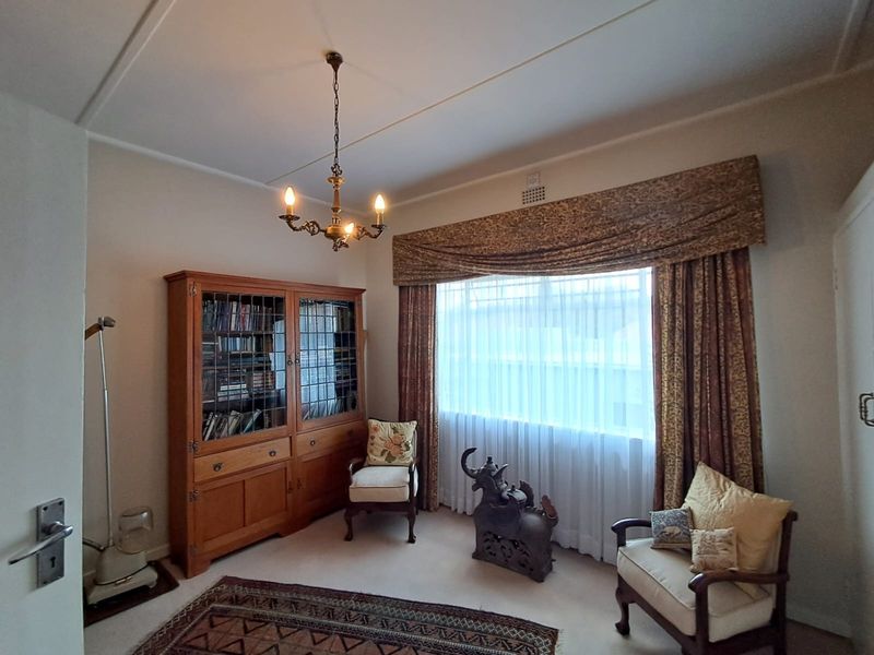 A cozy living room featuring a classic chandelier, built-in cabinetry, and a large window with decorative pelmet and curtains.