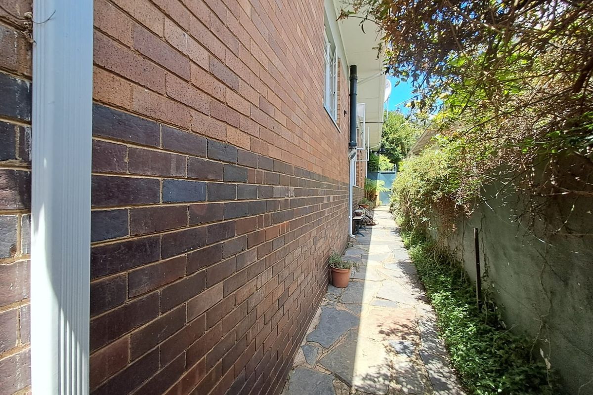 A side exterior view of the property featuring a brick facade, a stone paved pathway, and a retaining wall along the boundary.