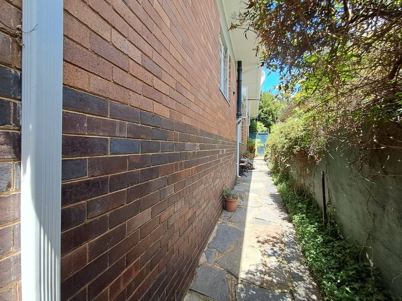 A side exterior view of the property featuring a brick facade, a stone paved pathway, and a retaining wall along the boundary.