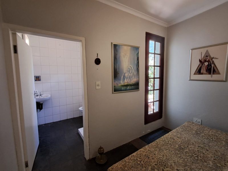 A bedroom featuring an en-suite bathroom with tiled flooring and a glass-paneled door providing access to the exterior.